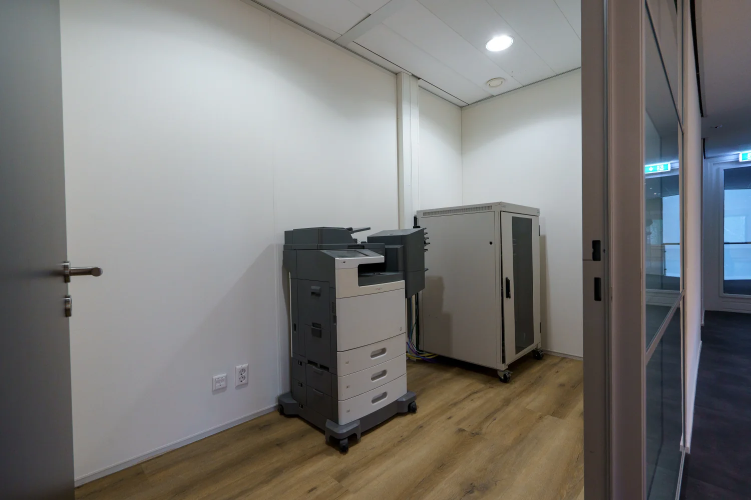 Kleine kantoorruimte aan de Baarnsche Dijk met een printer en serverkast op een houten vloer.